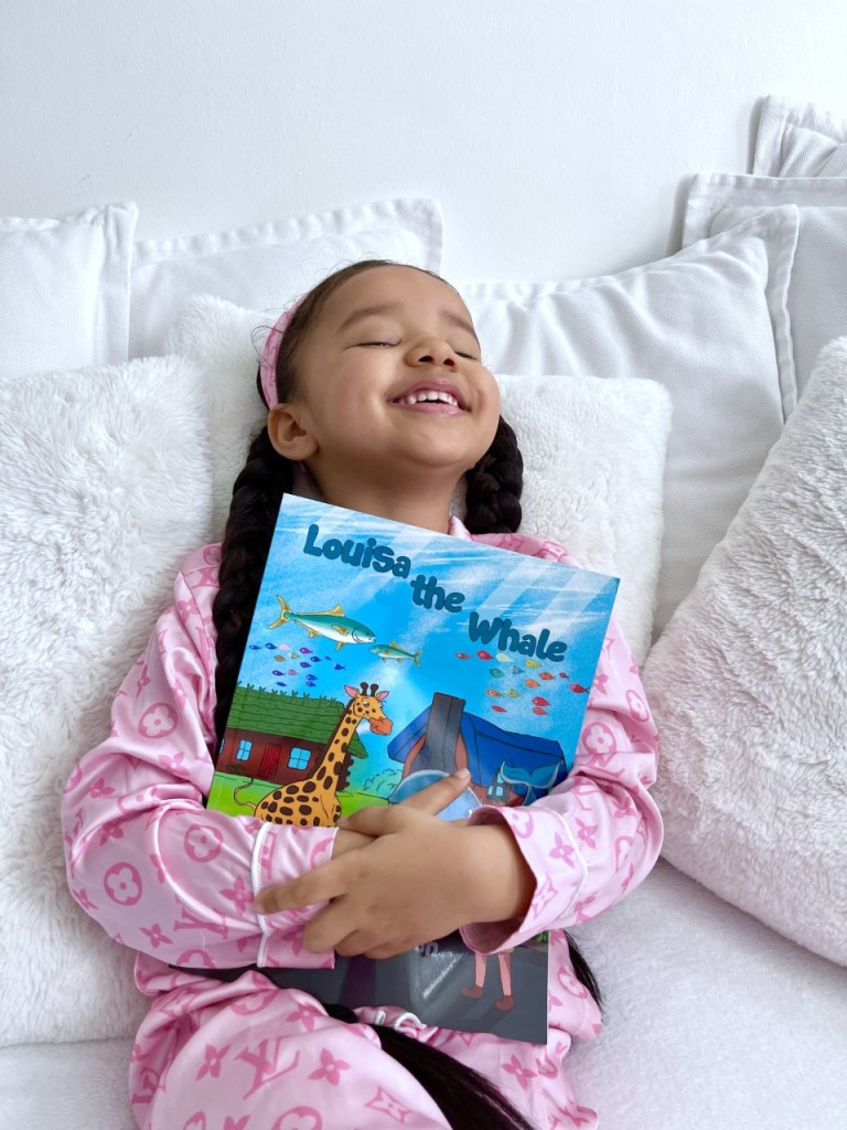 Lynnie is smiling, holding her new book in her hand, Louisa the whale. 